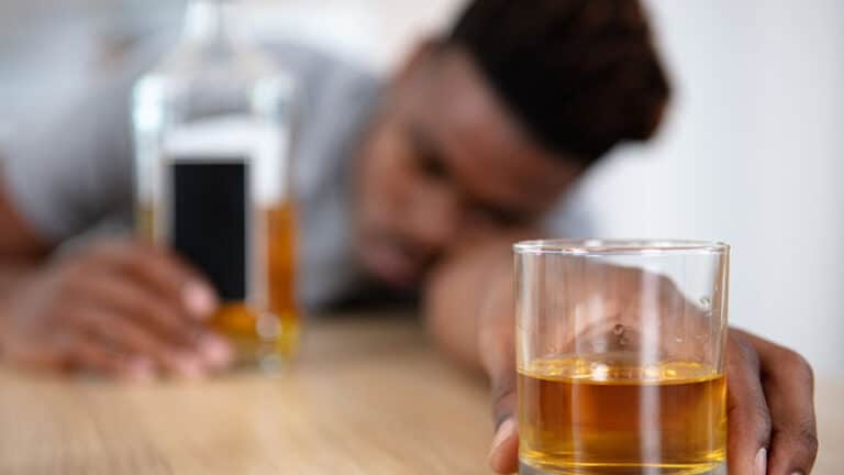 intoxicated man slumped table holding glass