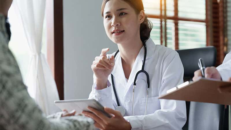 A doctor in a white coat converses with a patient