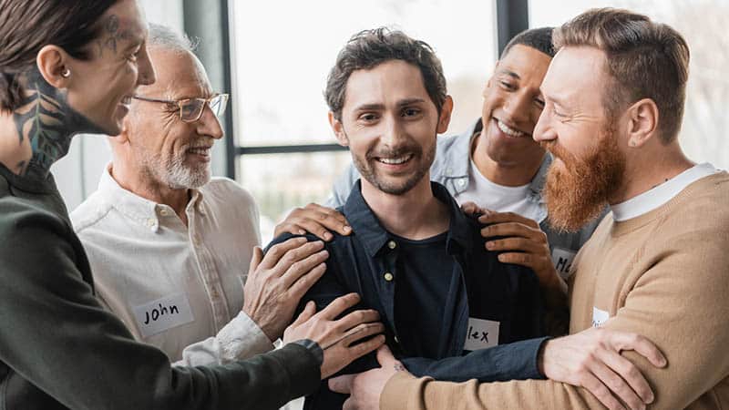 people hugging smiling man with alcohol addiction during group therapy