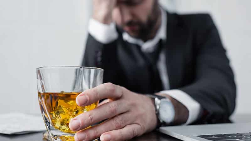male person sitting in the desk holding alcohol