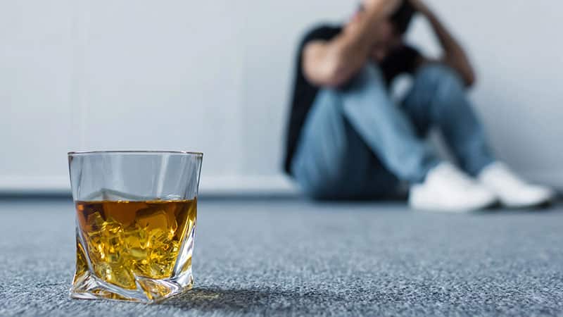 depressed man sitting floor wall glass whiskey