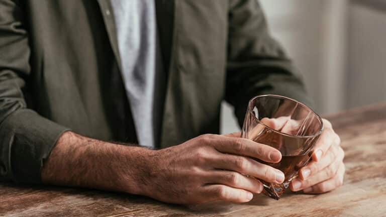man holding whiskey glass at table