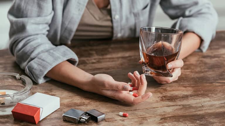 woman holding whiskey glass and pills