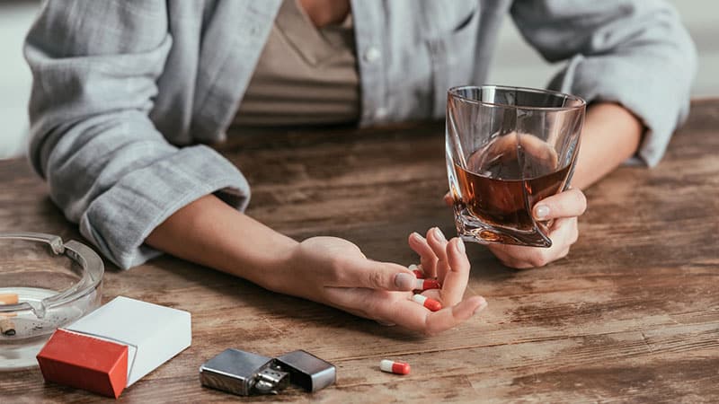 woman holding whiskey glass and pills