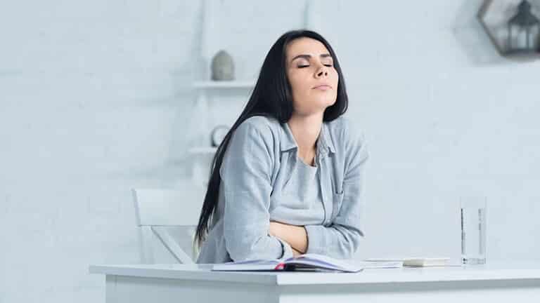 woman with closed eyes breathing while sitting at desk