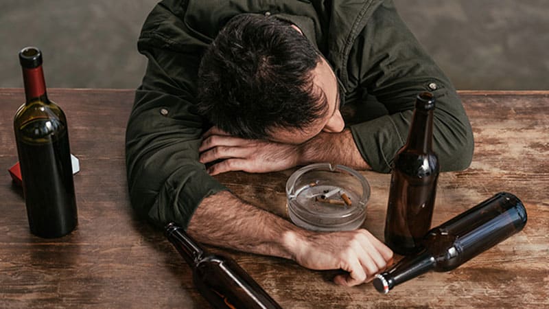 drunk man lying on table with bottles and ashtray