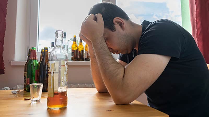 man sit next table drink alcohol bottle